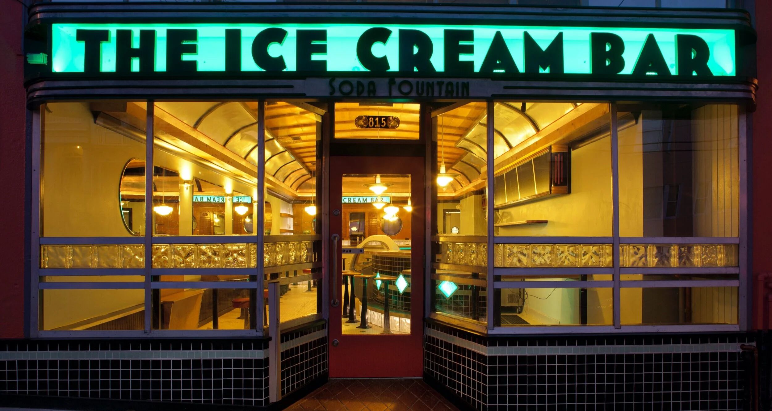 The lit shopfront at night under a sign reading THE ICE CREAM BAR