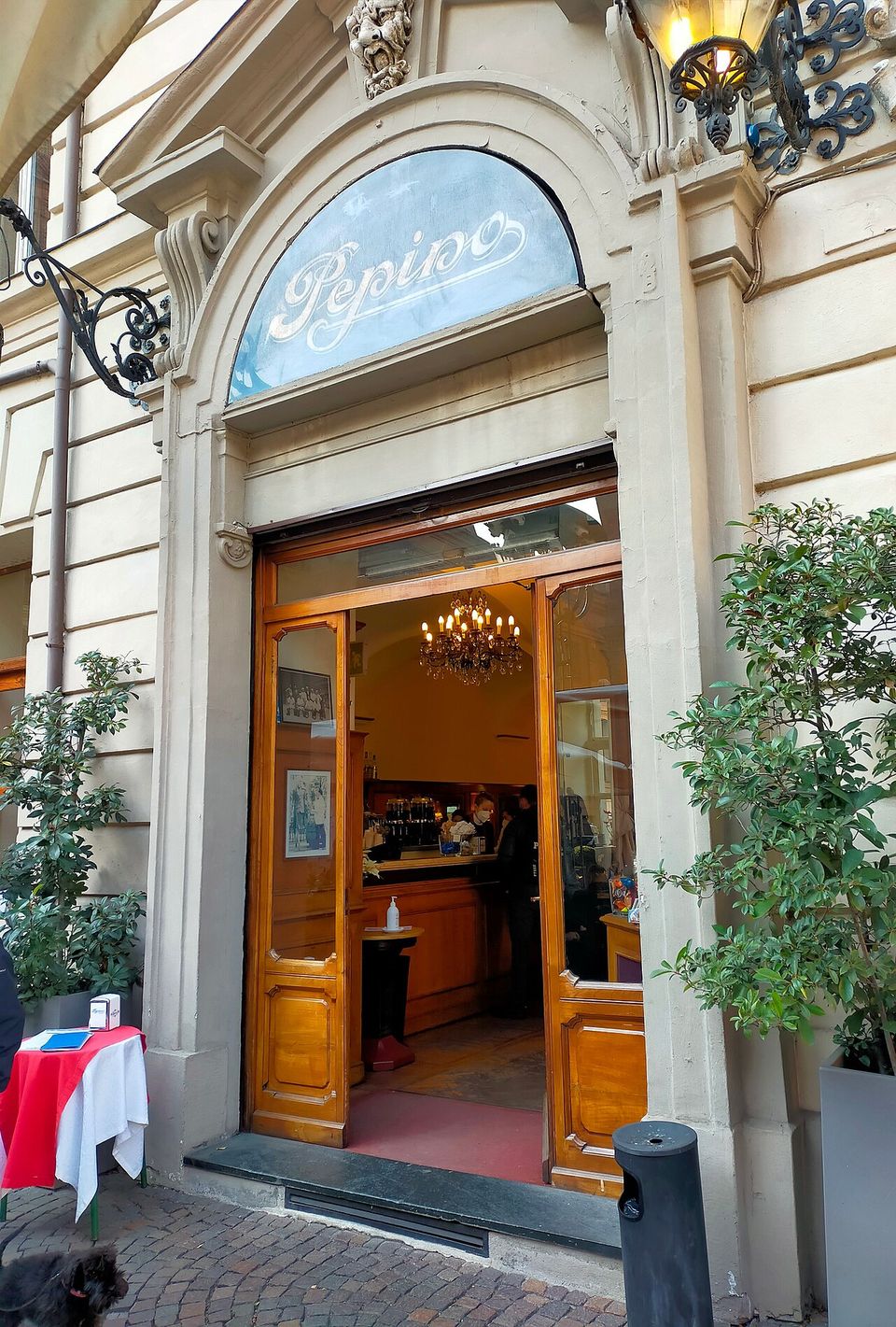 An arched doorway with Pepino painted in script across the fanlight, a chandelier and a wooden counter lit up inside