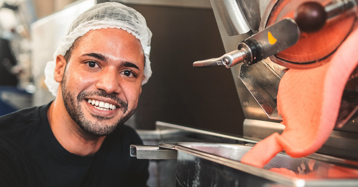 A worker in a hairnet smiling beside the production machine